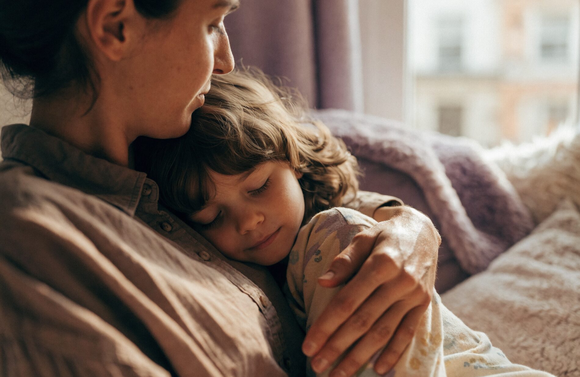 A parent holding their young child in a calm, reassuring embrace by a sunlit window